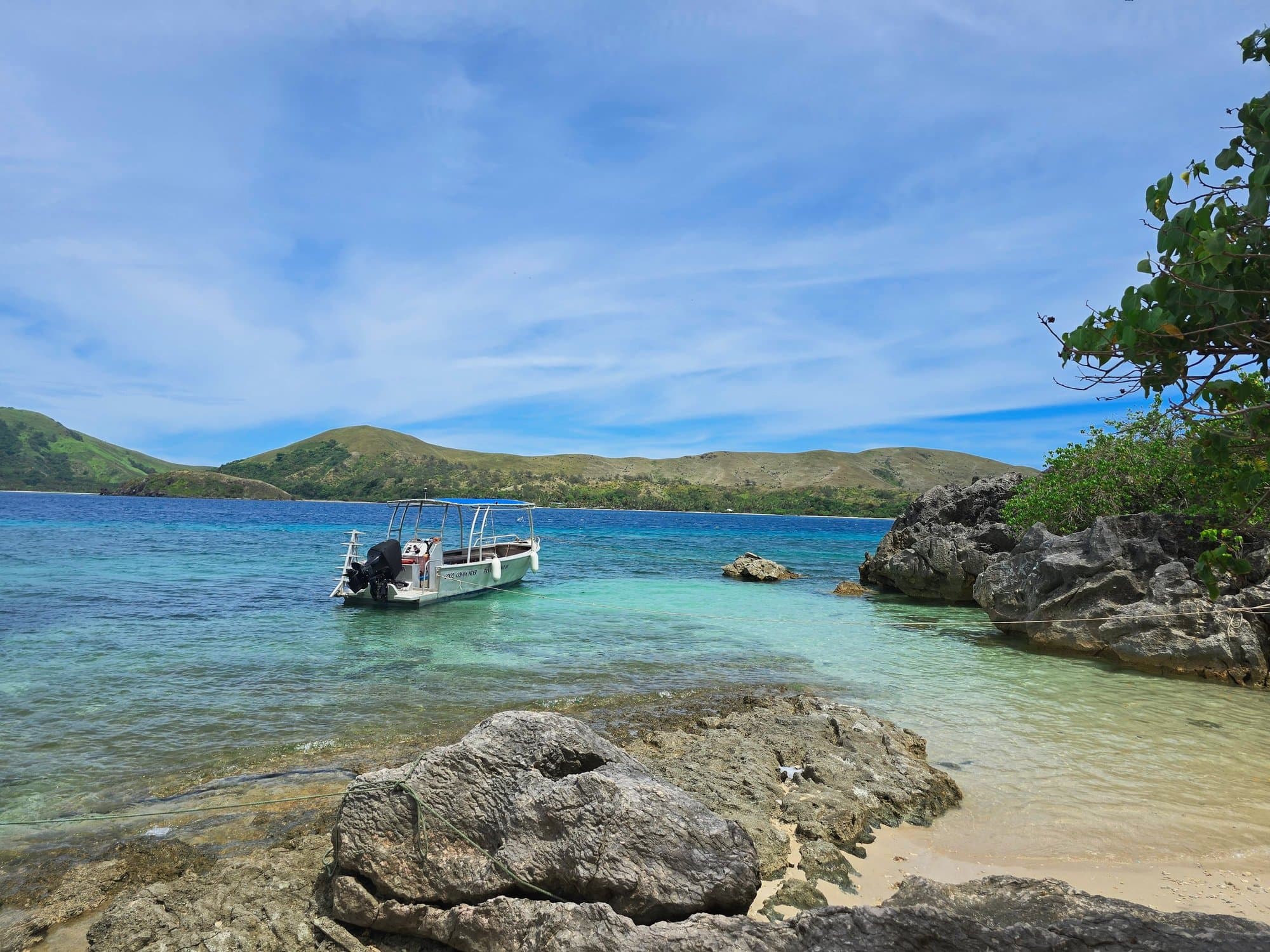 A small boat by limestone rocks in clear turquoise water in the northern Yasawas