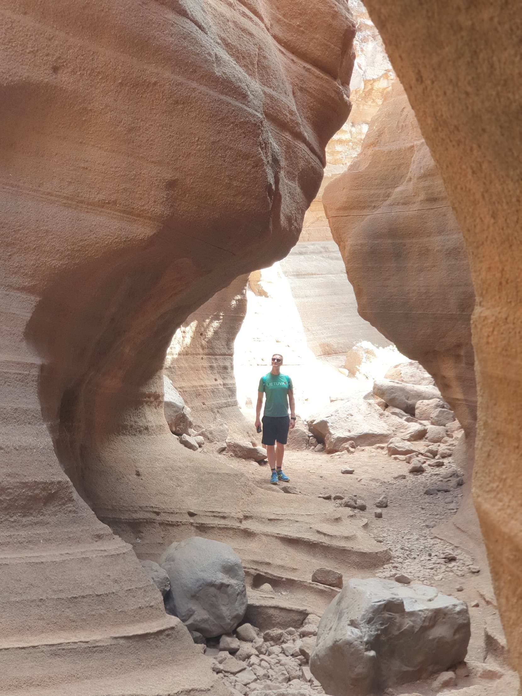 A figure standing under the curved terracotta arch of the Barranco de las Vacas slot canyon, Gran Canaria