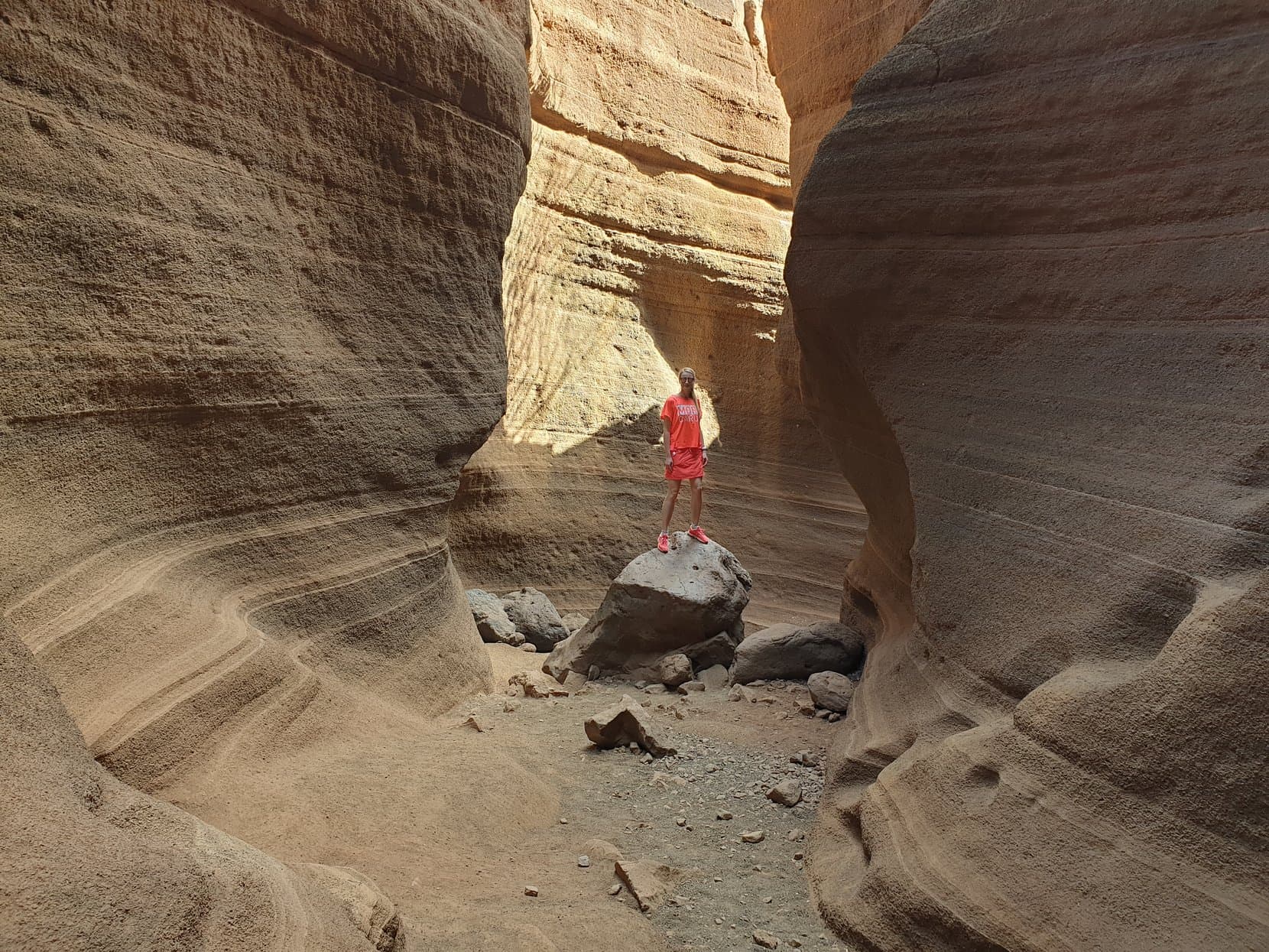 A figure in red between the curved walls of the Barranco de las Vacas slot canyon, Gran Canaria