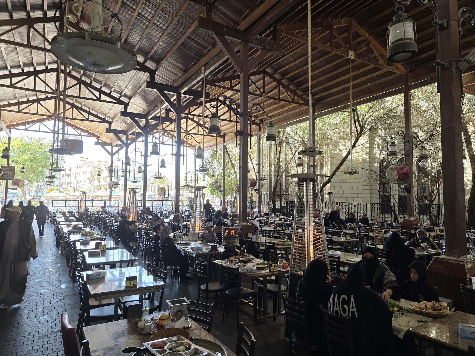 The open-air food courtyard of Souk Al-Mubarakiya under its timber roof, tables and heaters between the trees