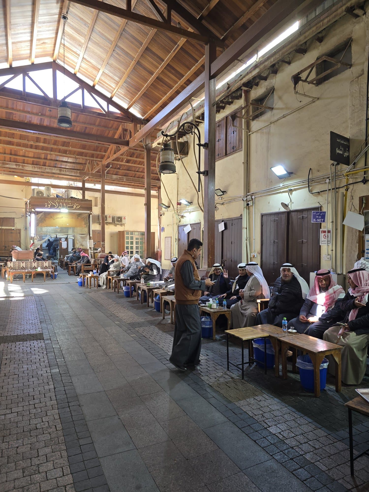 Men drinking tea on benches in a lane of Souk Al-Mubarakiya