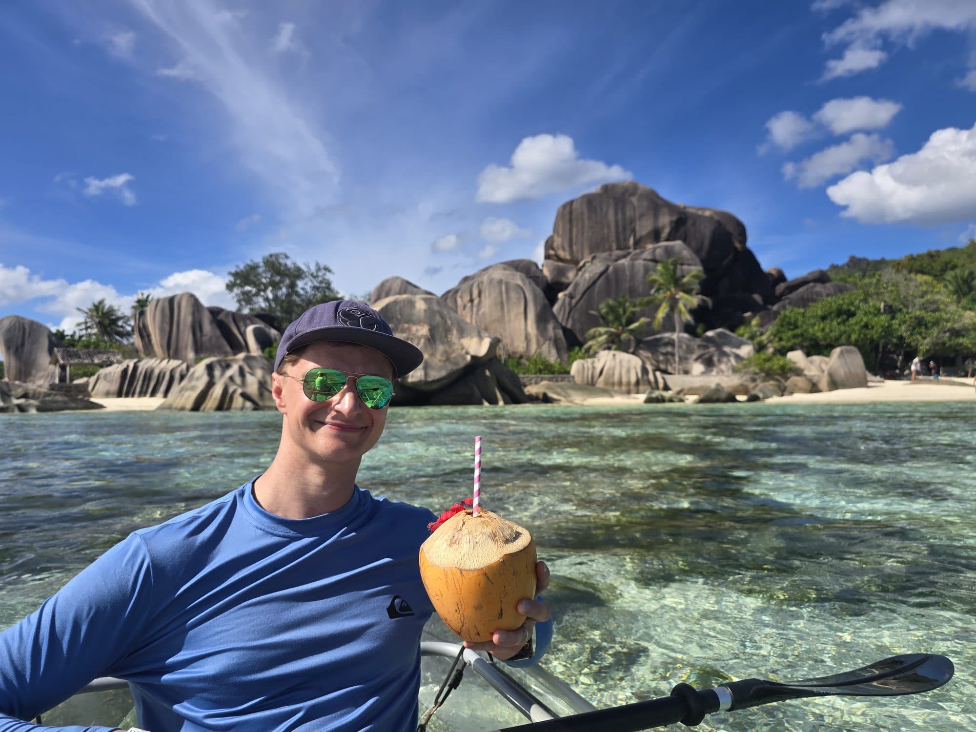 Holding a coconut from a kayak in front of the granite boulders of Source d'Argent, La Digue