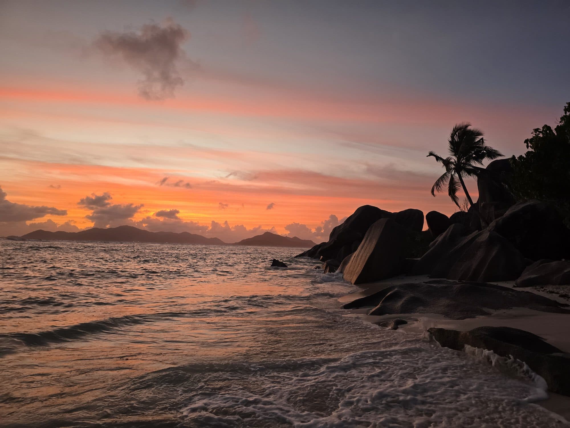 Sunset over the sea from the granite shore of Anse Source d'Argent, La Digue, Seychelles