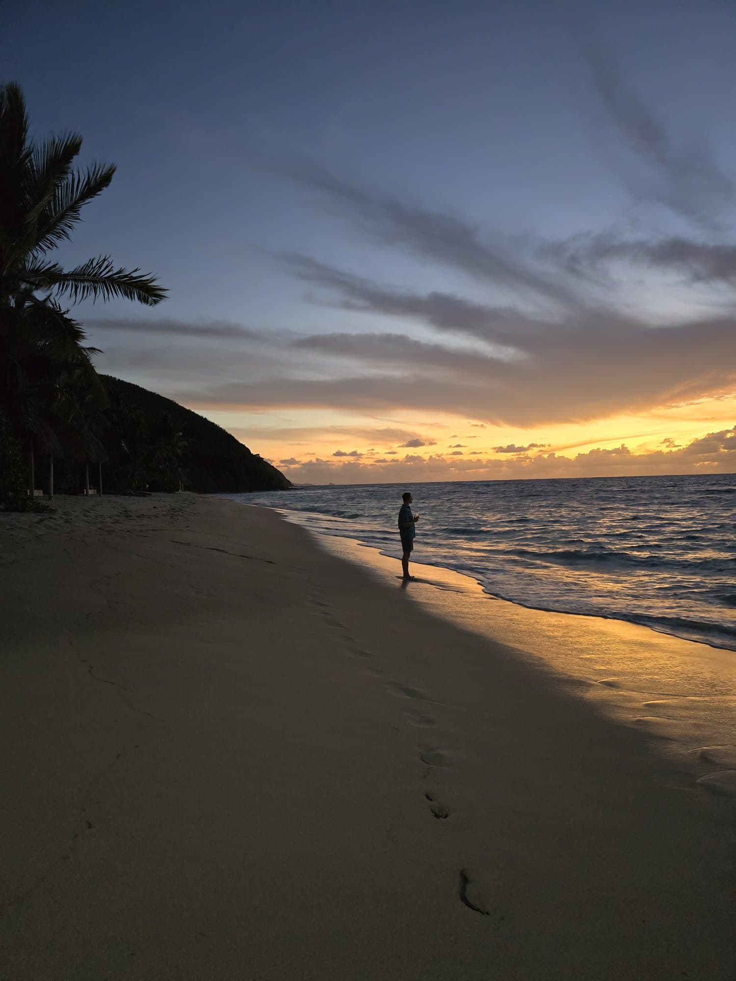 A figure walking an island beach at sunset