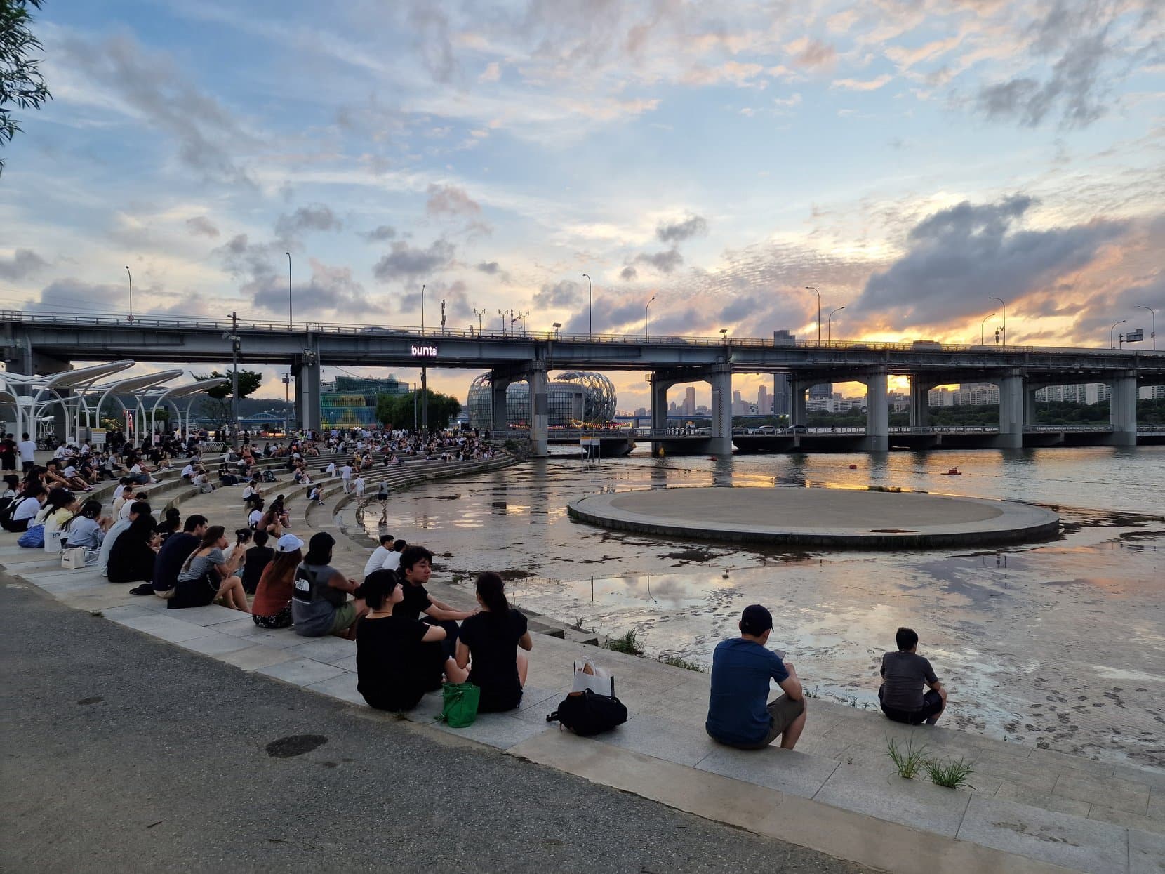 People sitting on the riverside steps under Banpo bridge at sunset, Han River, Seoul