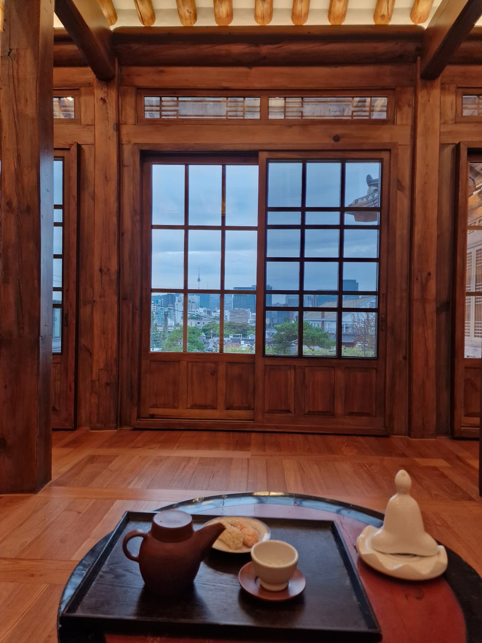 A tea tray on a low wooden table by a hanok window looking out over Seoul, Bukchon