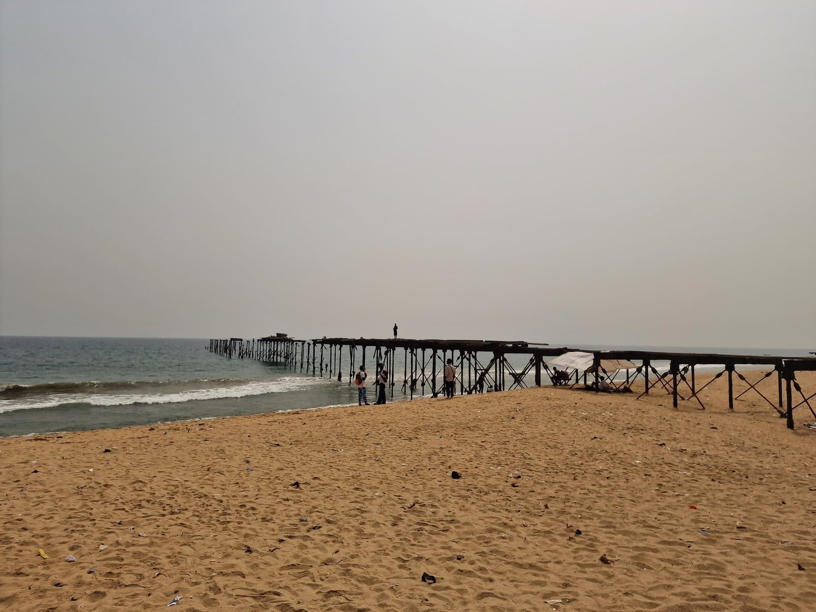 An old wooden pier running out into the surf from the sandy beach at Lomé, Togo