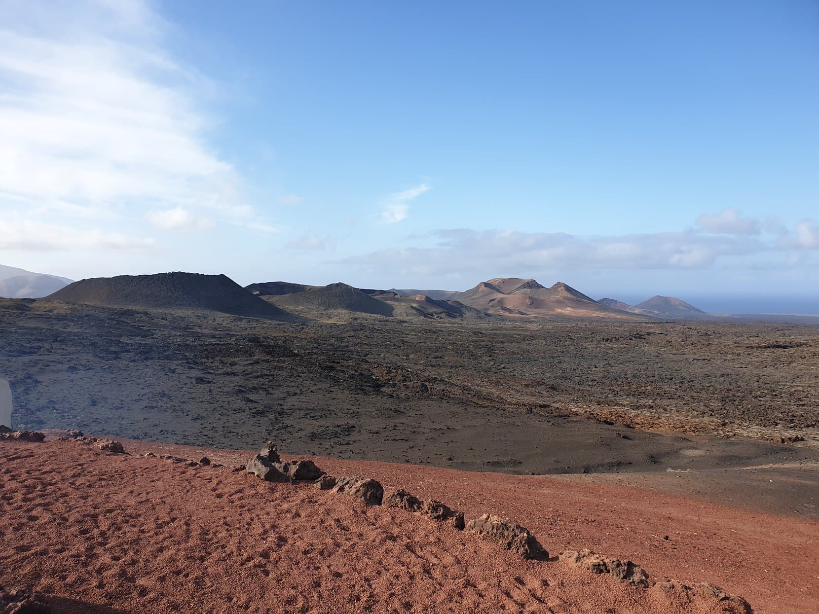 A black lava field with a red ash apron running to the volcano cones of Timanfaya, Lanzarote