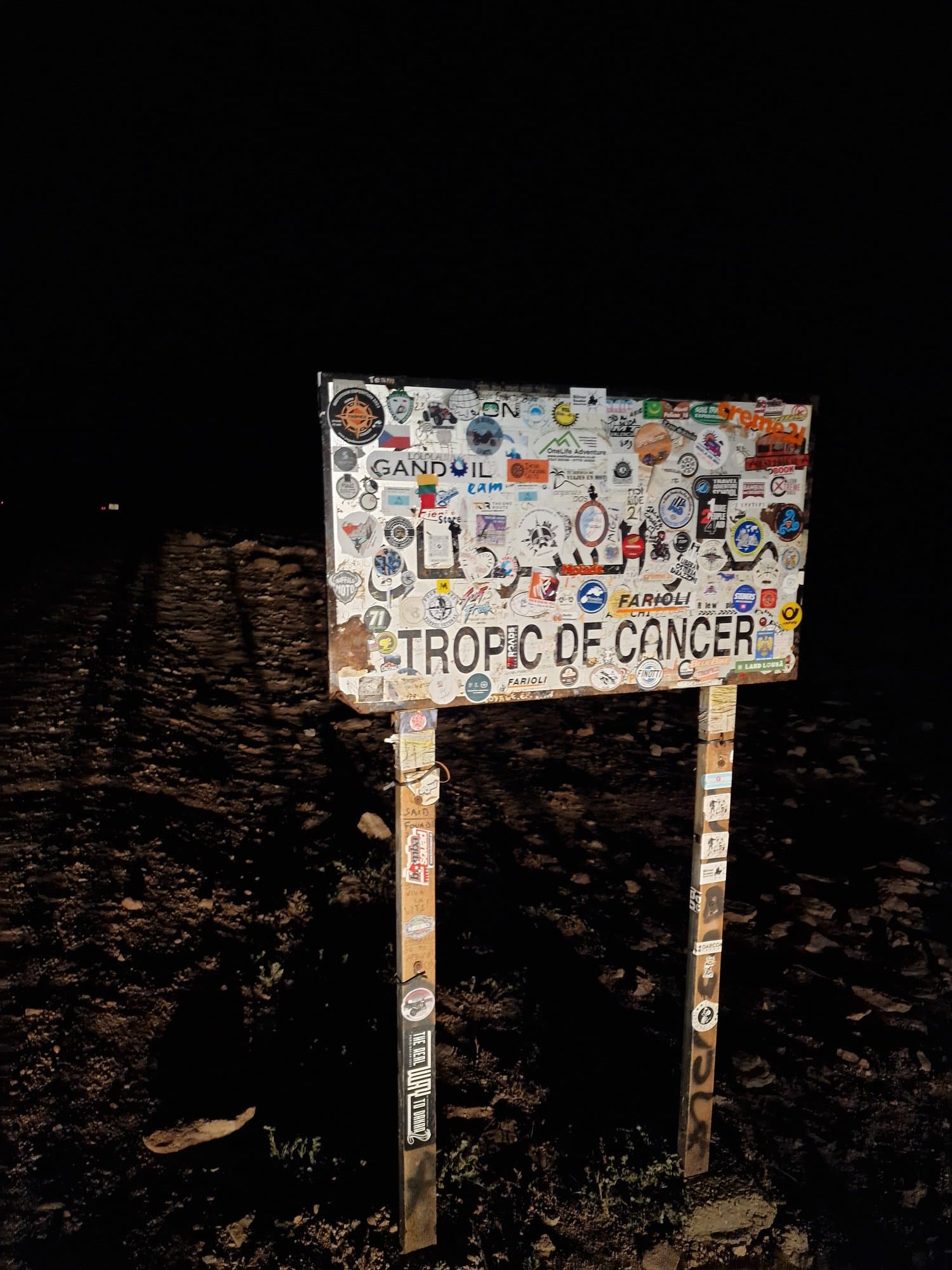 The sticker-covered Tropic of Cancer sign photographed at night