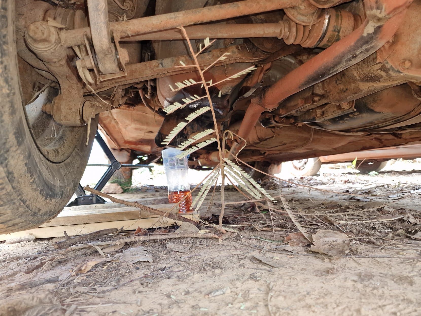 The underside of a jacked-up car showing the fuel tank and a bottle catching fuel
