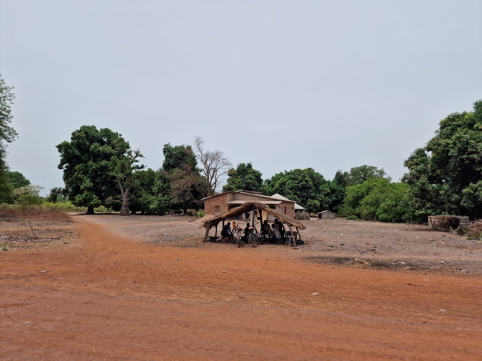 A village of round mud-walled houses with conical thatched roofs beside a red laterite road