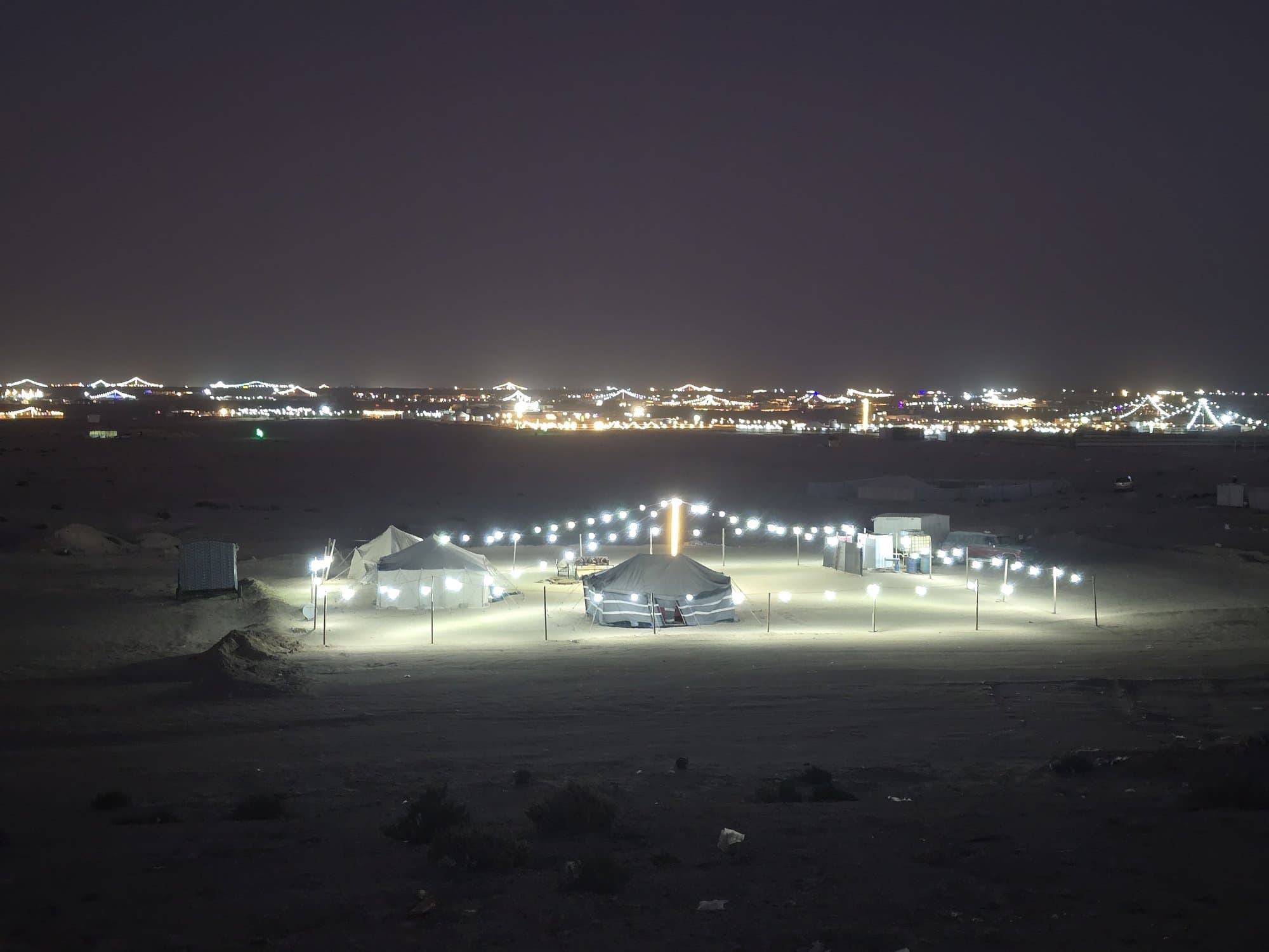 A winter tent camp lit up in the dark desert, seen from the road
