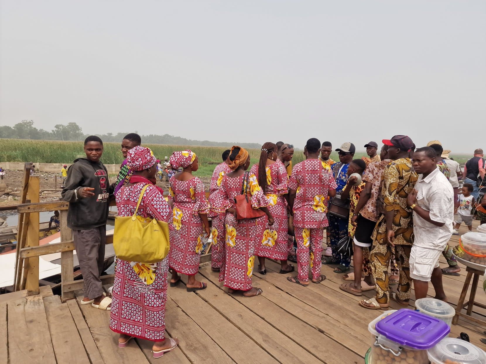 Women in matching printed cloth gathered on the wooden jetty at the Ganvié landing on Lake Nokoué, Benin