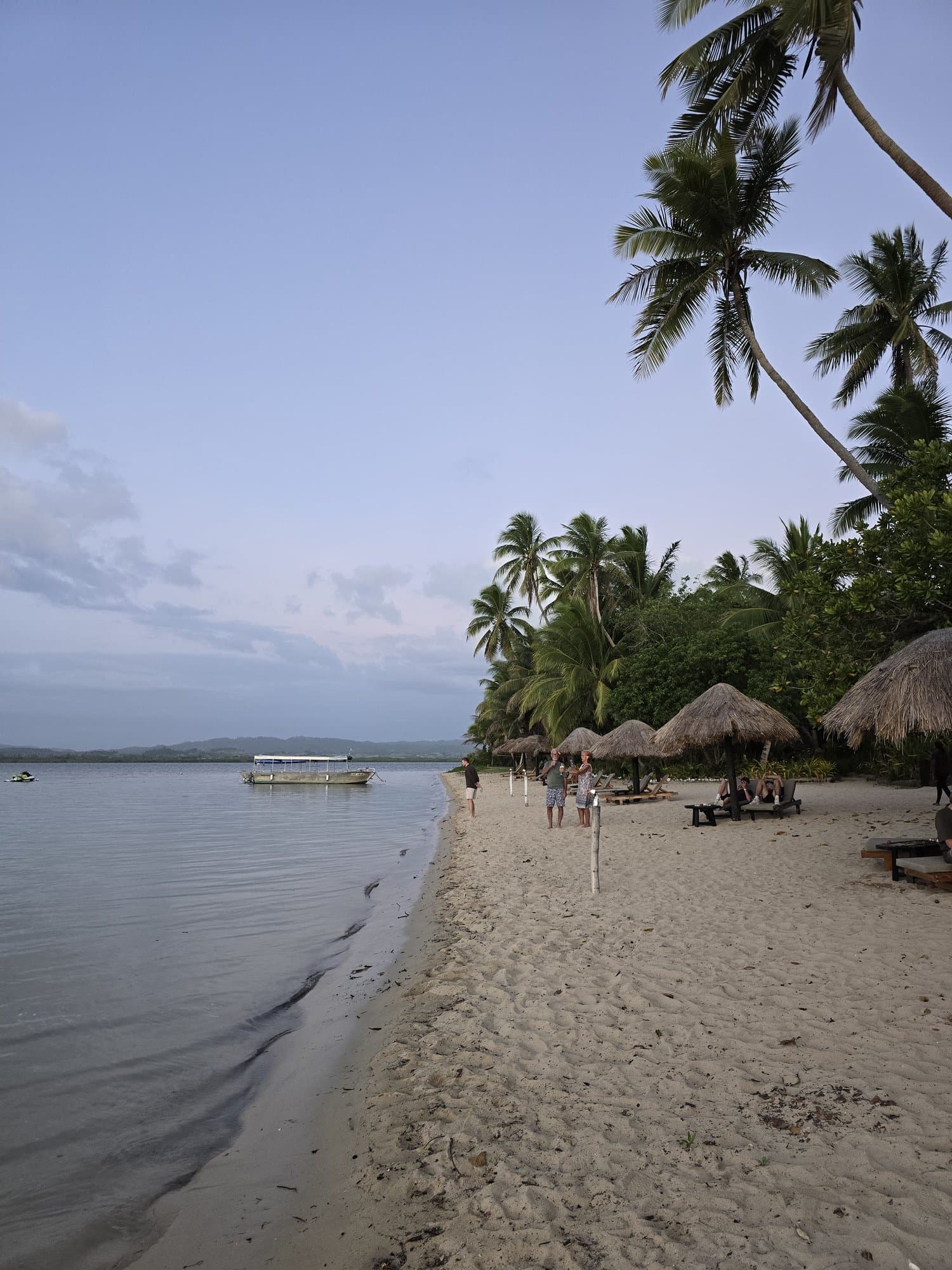 A long white-sand island beach with palms, walkers and boats offshore in the Yasawas