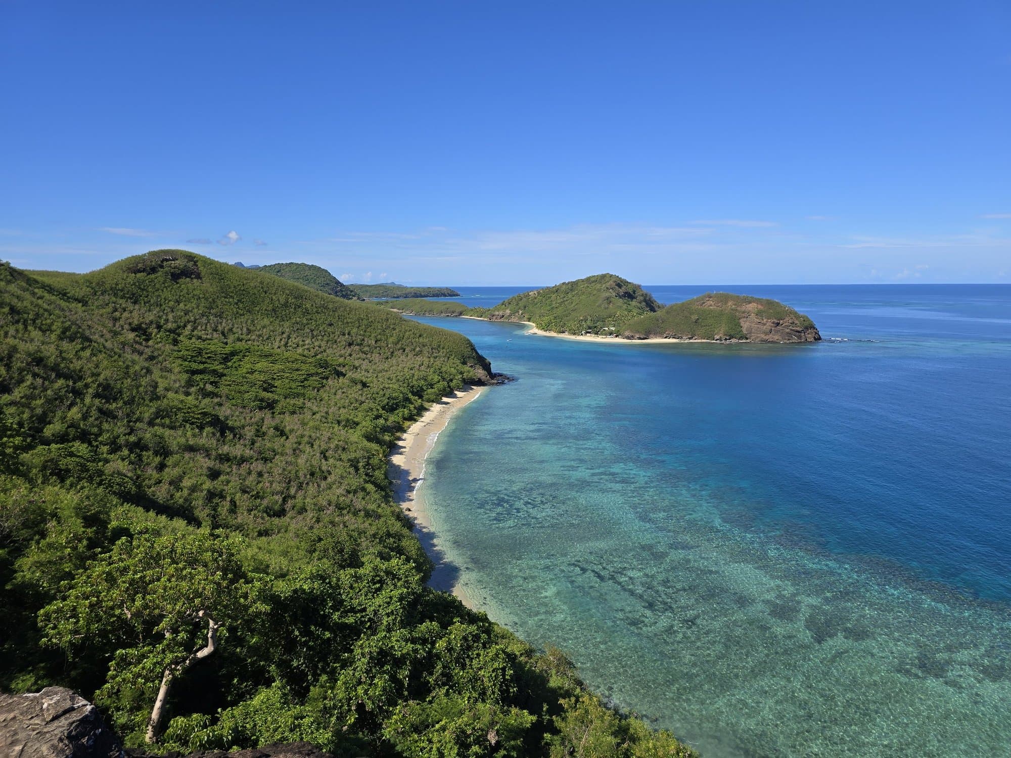 Looking down a green Yasawa island ridge to turquoise reef water and an offshore islet