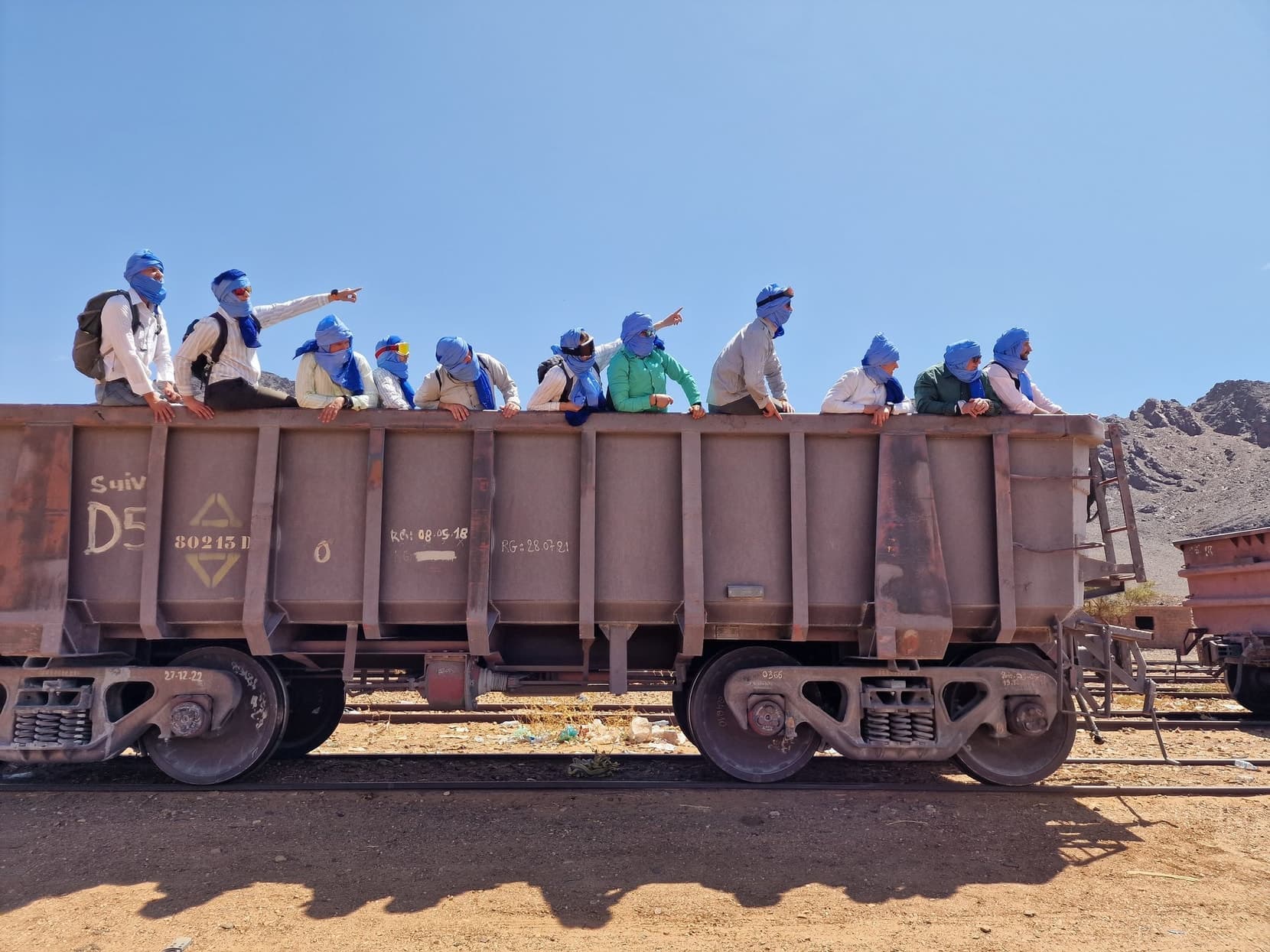 Travellers riding on top of an empty iron-ore wagon rake through the desert, Mauritania